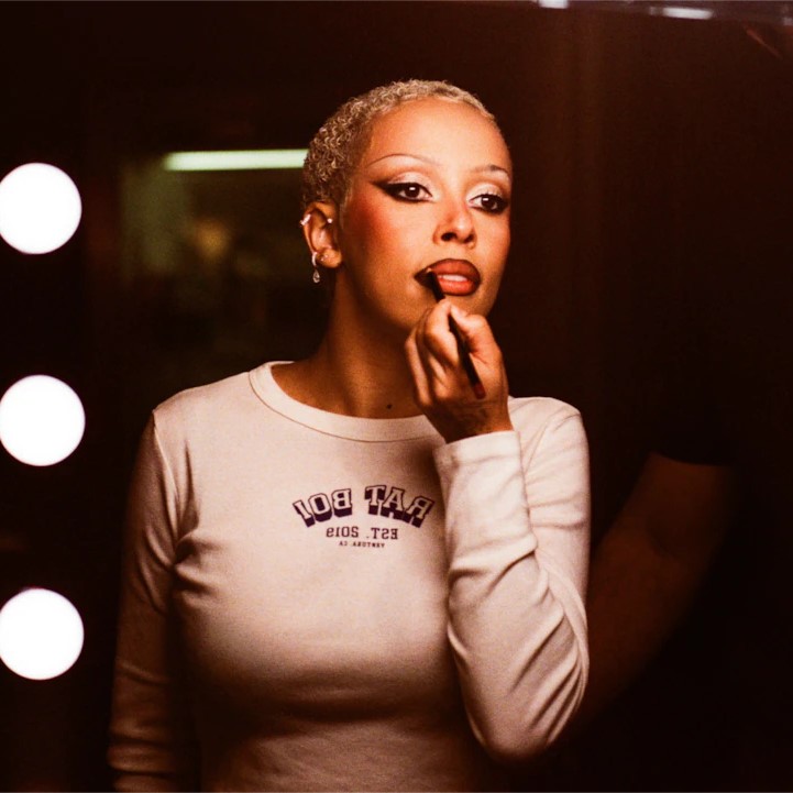 Singer Doja Cat looking into a mirror whilst applying lipstick.